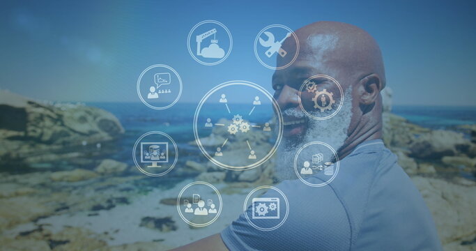 Image of media icons over smiling senior african american man at beach