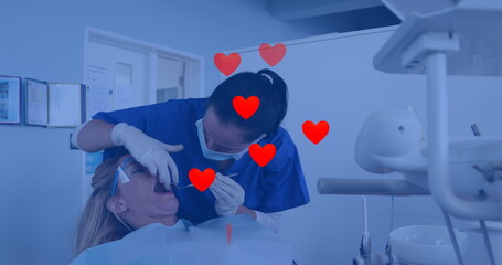 Image of heart icons over biracial female dentist treating caucasian woman - Powered by Adobe