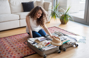 Beautiful woman planning summer vacation abroad, sitting on floor, packing suitcase. Solo traveler.