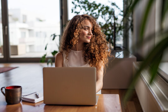 Beautiful woman working on laptop at home, homeoffice for young worker. Student studying at home, preparing for final exam.