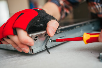 Detailed close-up of technician's hand in red glove using yellow screwdriver to tighten screw on metallic device, demonstrating precise mechanical work.