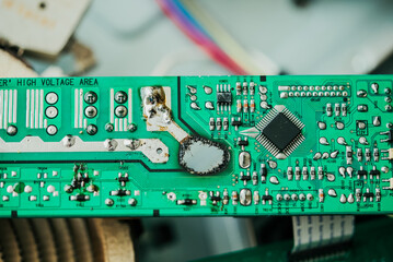 Detailed close-up shot of damaged electronic circuit board highlighting burnt components and intricate microchips on vibrant green background.