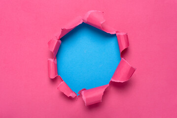 Tear hole in pink paper revealing a blue background. Space for text.