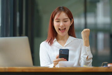 Asian businesswoman cheering while working on a laptop in an office.