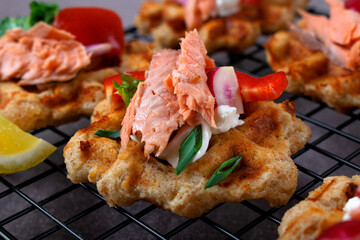 Cheese waffle topped with smoked trout, vegetables and sour cream sauce on the serving rack