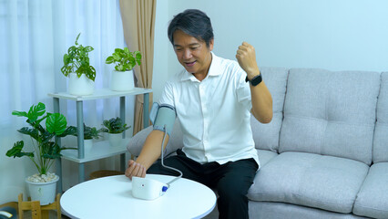 A middle aged asian man happy with measuring blood pressure at home health care concept.