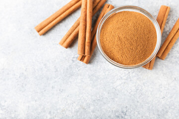 Cinnamon powder in a bowl on a textured wooden background. Spicy spice for baking, desserts and drinks. Fragrant ground cinnamon. Cinnamon stick. Place for text. Copy space.
