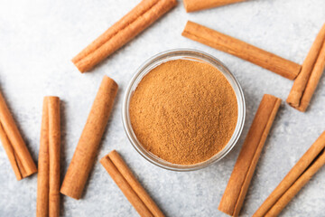 Cinnamon powder in a bowl on a textured wooden background. Spicy spice for baking, desserts and drinks. Fragrant ground cinnamon. Cinnamon stick. Place for text. Copy space.