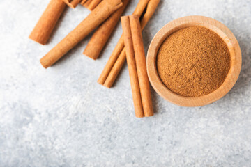 Cinnamon powder in a bowl on a textured wooden background. Spicy spice for baking, desserts and drinks. Fragrant ground cinnamon. Cinnamon stick. Place for text. Copy space.