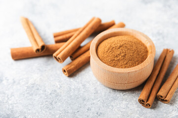 Cinnamon powder in a bowl on a textured wooden background. Spicy spice for baking, desserts and drinks. Fragrant ground cinnamon. Cinnamon stick. Place for text. Copy space.