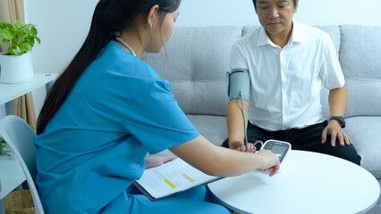 Asian female doctor taking notes about blood pressure Middle-aged Asian male patient at home.