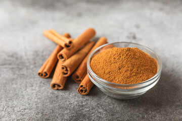 Cinnamon powder in a bowl on a textured wooden background. Spicy spice for baking, desserts and drinks. Fragrant ground cinnamon. Cinnamon stick. Place for text. Copy space.