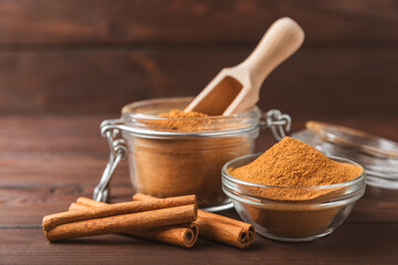 Cinnamon powder in a bowl on a textured wooden background. Spicy spice for baking, desserts and drinks. Fragrant ground cinnamon. Cinnamon stick. Place for text. Copy space.