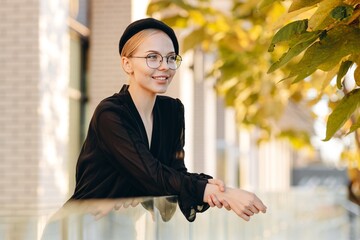 Happy beautiful girl with clear glasses on her eyes and a black beret on her head, wearing a black...