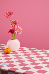 Advertising photo in pink color with a white flower vase of pink gerbera daisy next to an orange...