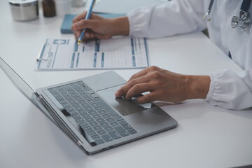 A professional and focused Asian female doctor in scrubs is working and reading medical research on...