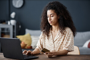 Young biracial woman sitting at desk in living room at home paying for goods in online store on...