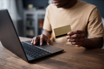 Crop shot of unrecognizable African American guy holding credit card buying goods in online store on laptop