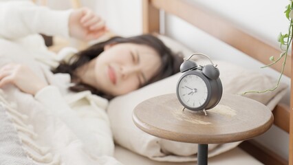 目覚まし時計に起こされる女性