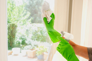 Close-up of a woman's hand cleaning and wiping window with spray bottle at home