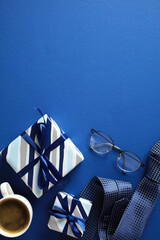 Gift Set on Blue. Top view of a neat gift arrangement with two wrapped presents, eyeglasses, a coffee cup, and a rolled tie on a elegant blue background. Ideal for gifting and celebration themes.