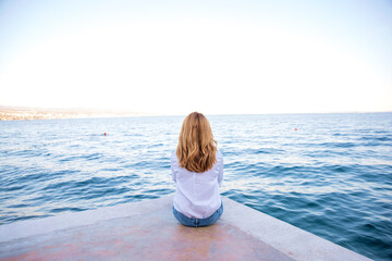 Rear view of a middle-aged woman sitting on the pier and enjoying the view of the sea