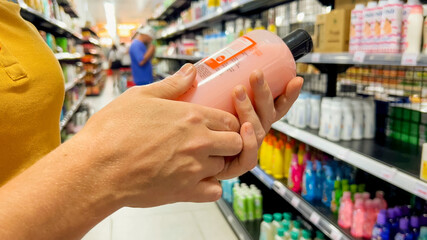 Person examining a bottle of body wash in the hygiene products aisle at a store, conceptually...