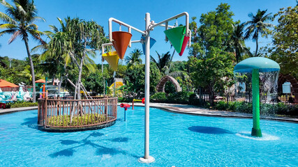 Sunny day at a tropical water park featuring colorful tipping buckets and a sprinkler mushroom,...