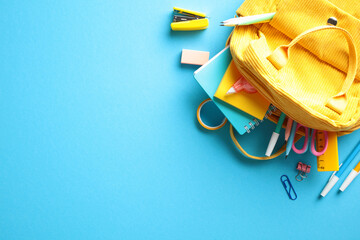 Yellow backpack with colorful school supplies, notebooks, pens, pencils, markers, scissors, eraser,...