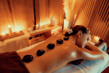 Hot stone massage at spa salon in luxury resort with warm candle light, blissful woman customer...