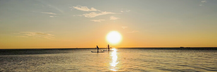 Two people paddleboarding on a calm ocean at sunset, silhouetted against the golden sky  ideal for summer vacations and water sports concepts