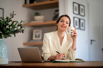 Young woman with laptop sitting at desk at home and working