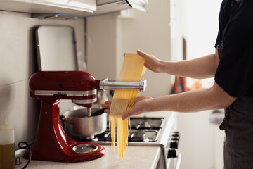 Person using a red kitchen mixer to make fresh homemade pasta in a cozy kitchen setting.