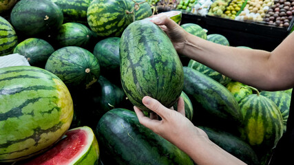 Person selecting fresh watermelons at a local farmers market, depicting healthy eating and summer harvest, ideal for National Watermelon Day promotions