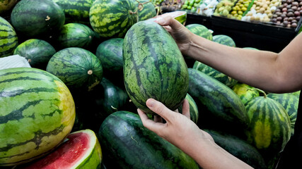 Person selecting fresh watermelons at a local farmers market, depicting healthy eating and summer...