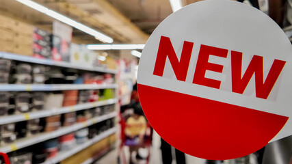Round 'New' sign in a store aisle indicating fresh merchandise arrivals, ideal for retail marketing...