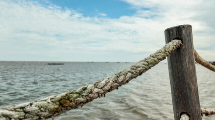 Close-up of weathered rope on wooden post at seaside, evoking summer, travel, and tranquility,...