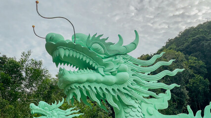 Vibrant green dragon sculpture against a cloudy sky, symbolizing Chinese culture, ideal for Lunar...