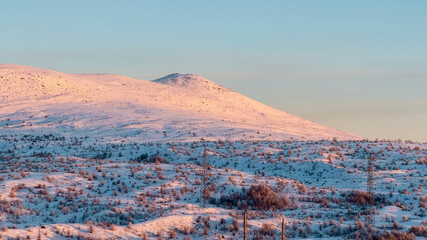 Gentle sunrise over a snow-covered hillside landscape, depicting a serene winter morning, ideal for...