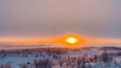 Scenic winter sunset with snow-covered trees under a vibrant orange sky, ideal for Christmas and...