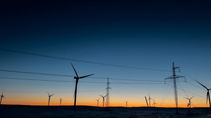 Sustainable energy concept with silhouette of wind turbines at sunset in a snowy landscape, ideal for environmental awareness campaigns and Earth Day promotions