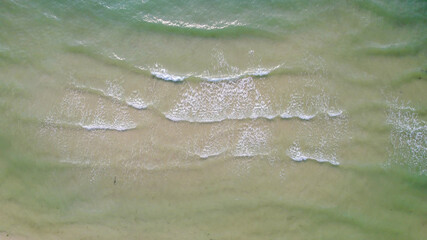 Serene aerial view of gentle sea waves washing over a sandy beach, ideal for travel themes and...