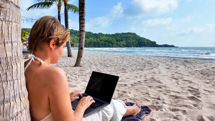 Caucasian woman using a laptop on a tropical beach with palm trees, embodying leisure technology use and summer vacations, freelancer, digital nomad