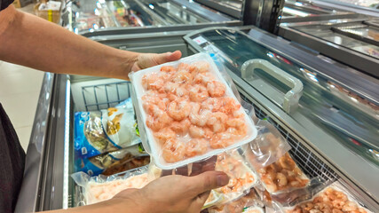 Shopper selecting a packaged fresh shrimp at a seafood section in a supermarket, ideal for culinary...