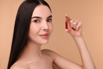 Beautiful young woman holding skincare ampoule on beige background