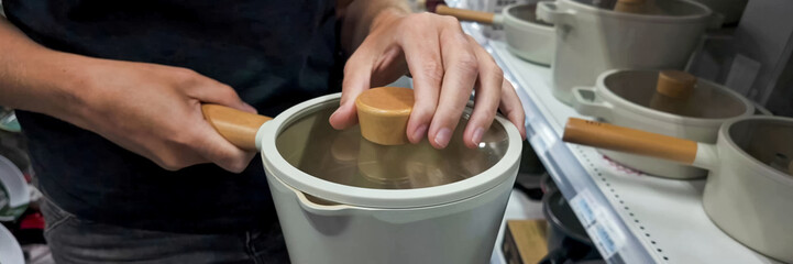 Person using a wooden utensil to open a modern rice cooker amidst kitchenware, depicting everyday...