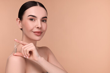 Beautiful young woman holding skincare ampoule on beige background. Space for text