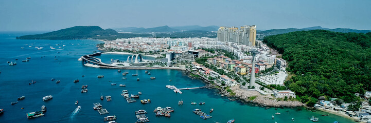 Aerial view of a bustling coastal city with modern architecture and a marina, ideal for travel,...