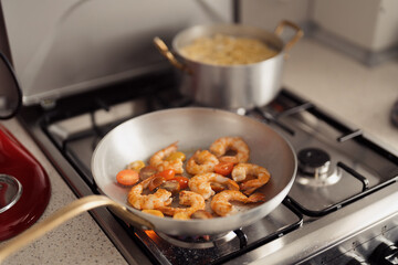 Shrimp being sauteed with tomatoes in a modern kitchen setting.