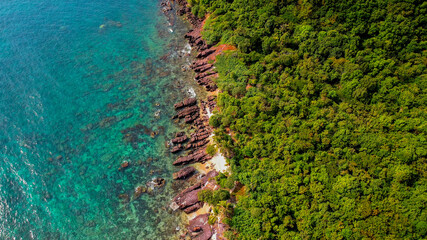 Aerial view of a rugged coastline with red rock formations and lush greenery meeting the turquoise sea, suitable for Earth Day and nature conservation topics